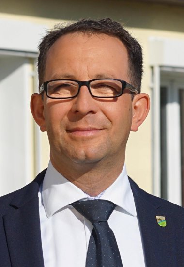 Bürgermeister steht fröhlich vor der Gemeindeverwaltung der Gemeinde Nuthe-Urstromtal