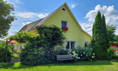 Ferienwohnung Lotte in Felgentreu gelbes Haus mit einer Bank davor, umrahmt von Blumen, Büschen und Bäumen