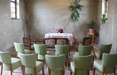 Trauraum im alten Güterschuppen großer, alter Raum mit hoher Decke, zwei Fenstern, einem Tisch und grünen Stühlen