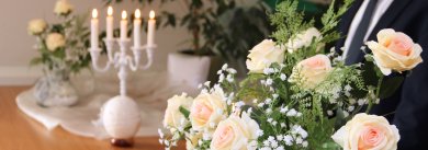 Standesamt Blumen und ein weißer Kerzenständer mit weißen, brennenden Kerzen stehen auf einem Tisch