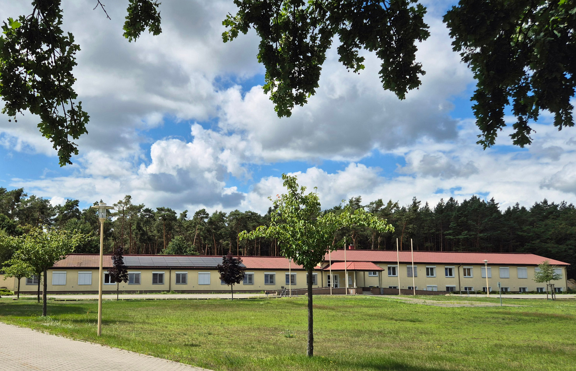langgestrecktes, flaches Gebäude mit Wald dahinter und einer grünen Wiese davor
