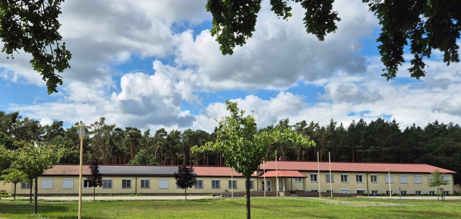 Gemeindeverwaltung in Ruhlsdorf langgestrecktes, flaches Gebäude mit Wald dahinter und einer grünen Wiese davor